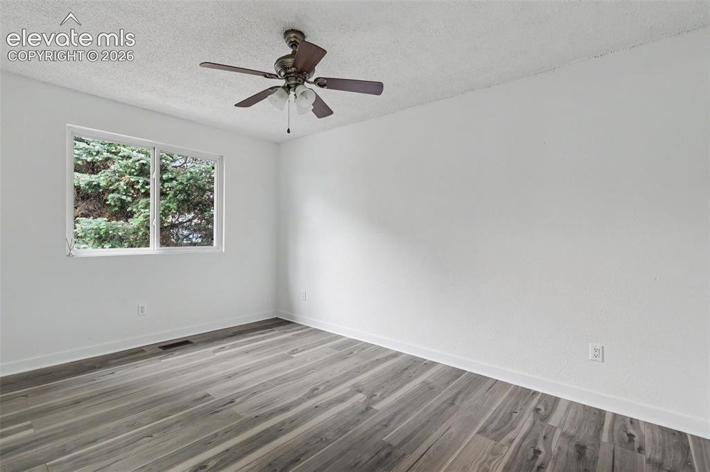 Image 27 of 43: Spacious room featuring wood-finish flooring, white walls, and a ceiling fa