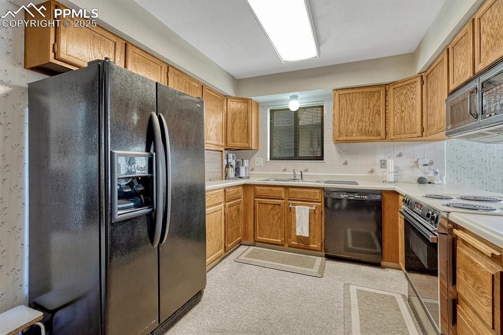 Image 12 of 46: Kitchen with black appliances, brown cabinetry, light countertops, and tast
