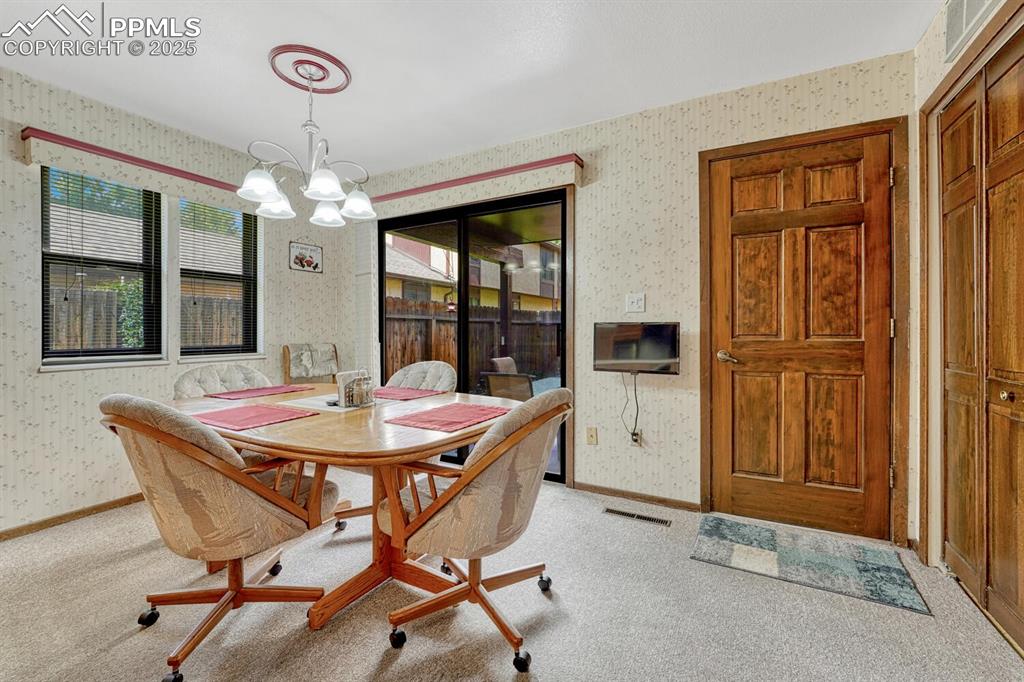 Image 15 of 46: Dining area featuring wallpapered walls, light colored carpet, and a chande
