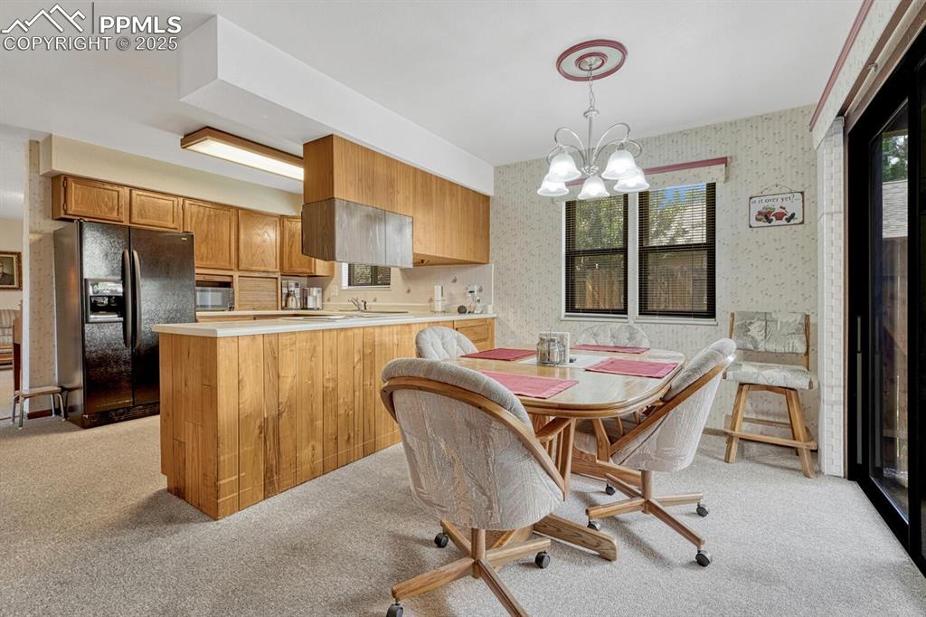 Image 17 of 46: Dining area with wallpapered walls, light carpet, and a chandelier