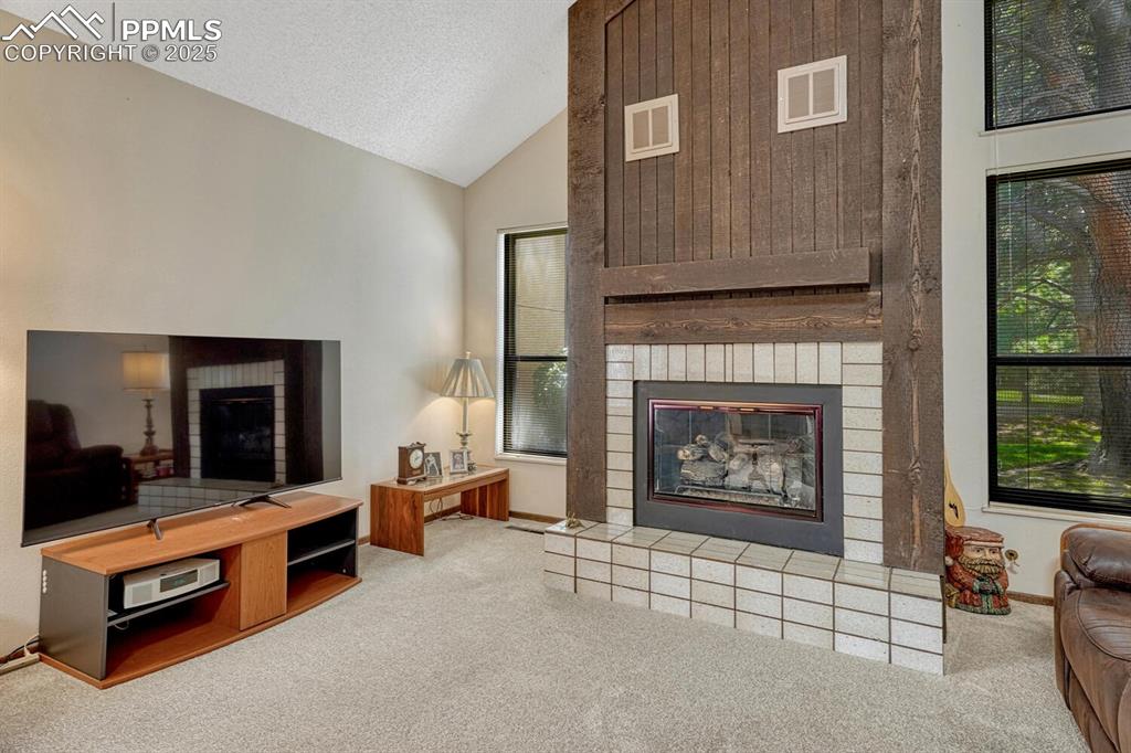 Image 4 of 32: Living area featuring a brick fireplace, vaulted ceiling, a textured ceilin