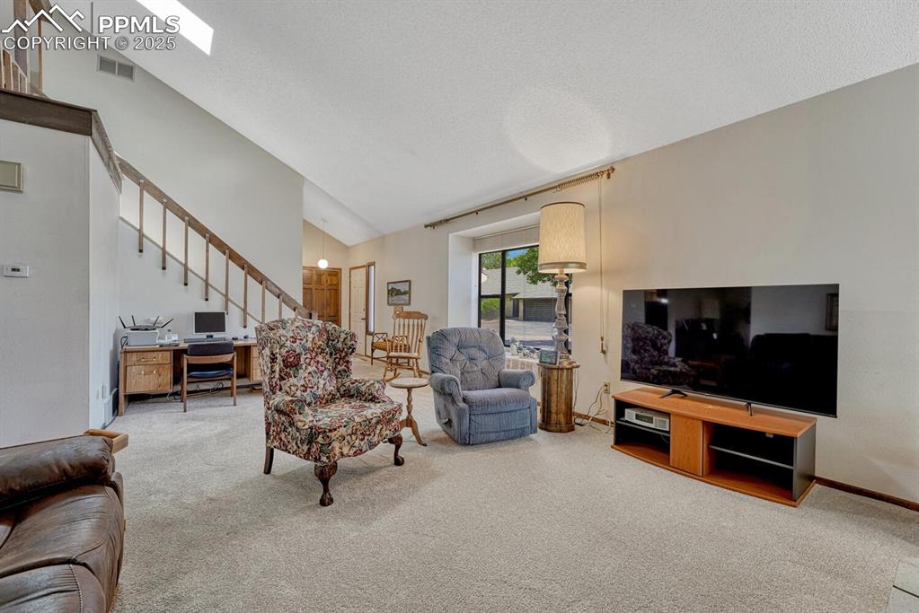 Image 5 of 46: Living room featuring carpet floors, stairway, a textured ceiling, high vau