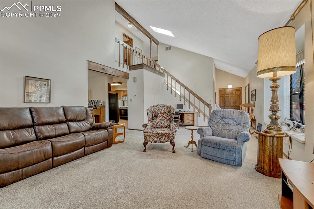 Image 6 of 46: Carpeted living area with high vaulted ceiling and stairway