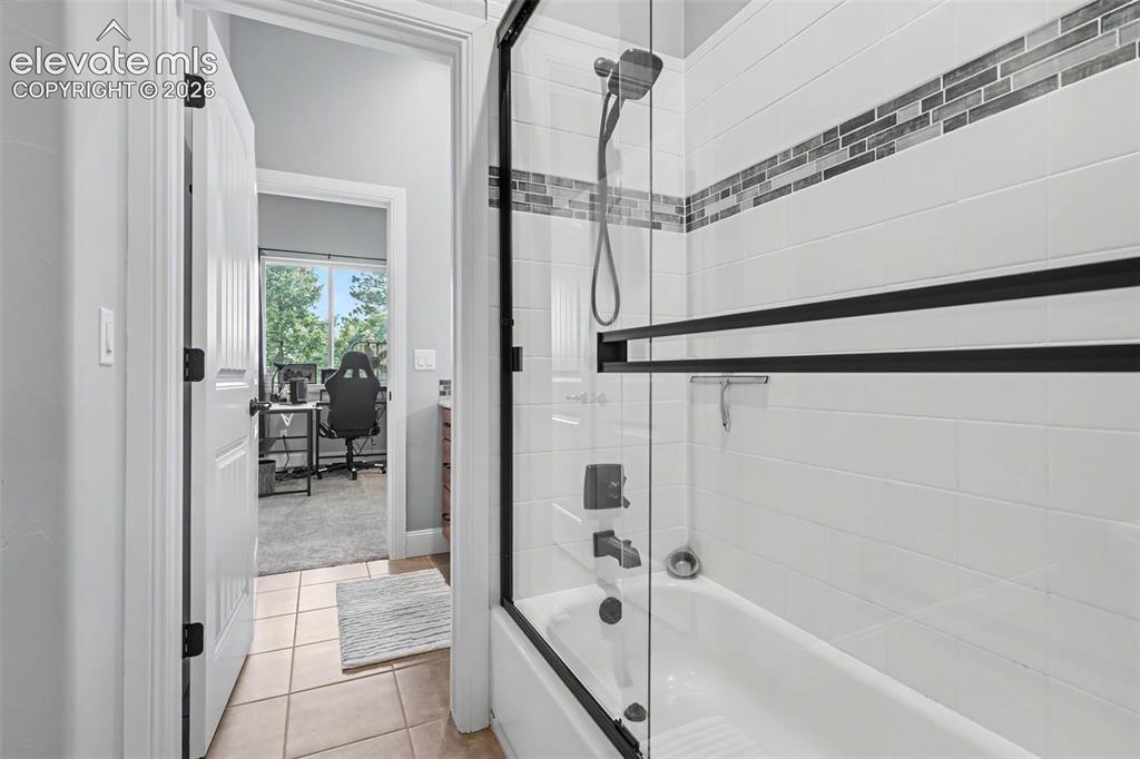 Image 44 of 48: Bathtub with a glass shower enclosure featuring matte black hardware, white