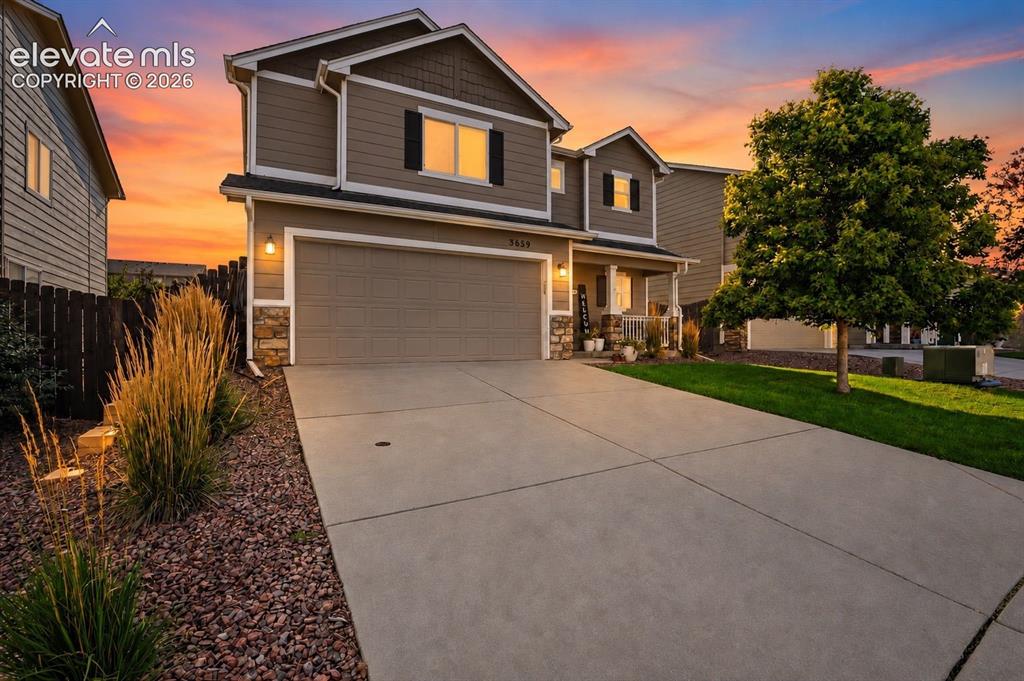 Caption: Two-story property featuring a front-facing garage door, a covered porch entry, and stone accents