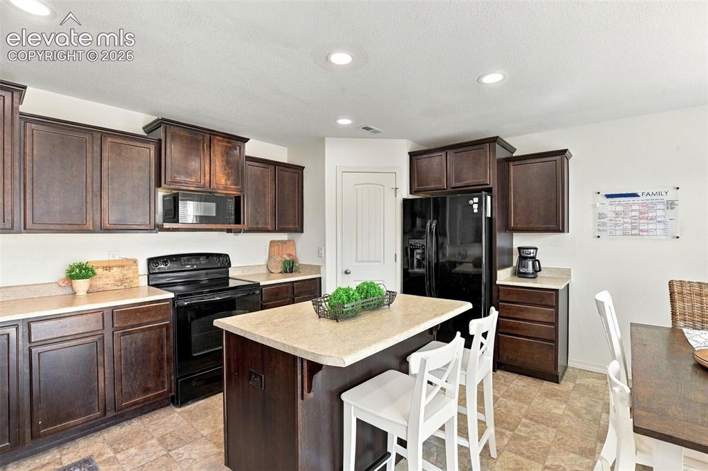Image 12 of 48: Kitchen featuring dark wood cabinetry, a central island with countertop sea