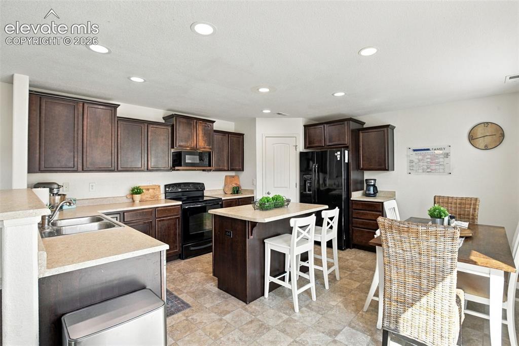 Image 13 of 48: Kitchen featuring dark wood-finish cabinetry, black appliances, a central i
