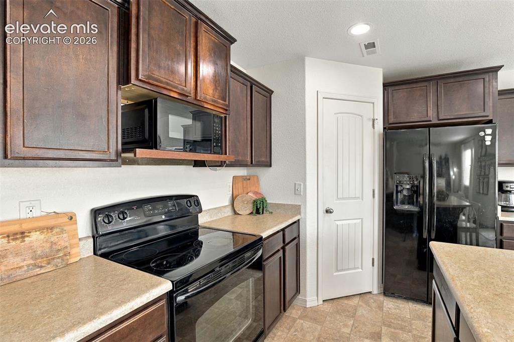 Image 15 of 48: Kitchen featuring dark wood-finish cabinetry, light-toned countertops, blac