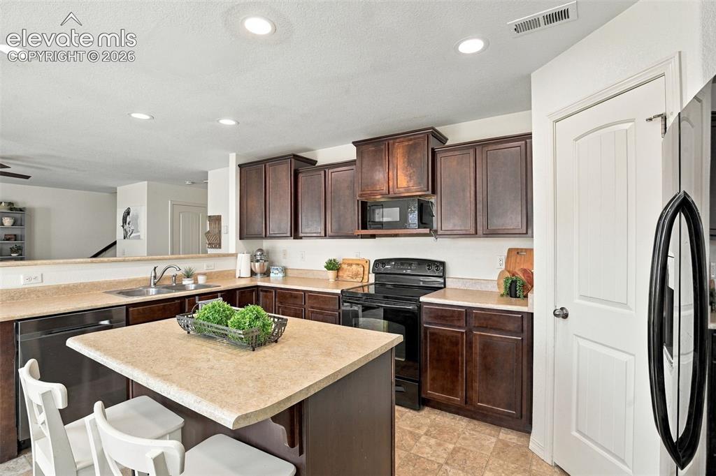 Image 19 of 48: Kitchen featuring dark wood cabinetry, light-toned countertops, a stainless