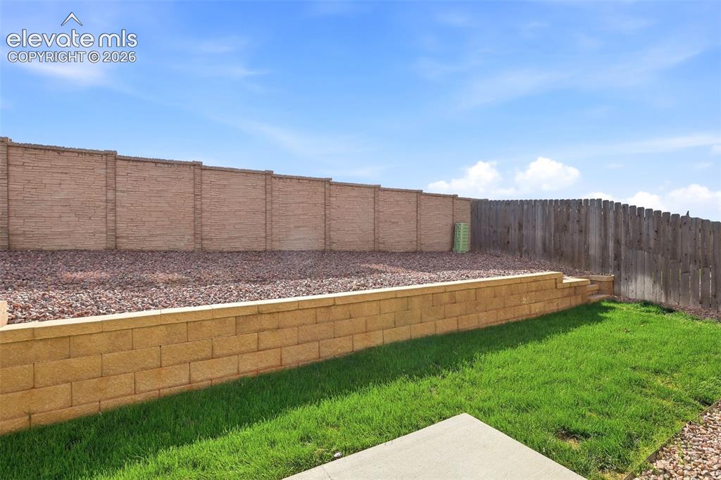Image 42 of 48: Tiered backyard landscaping featuring a block retaining wall, a full privac