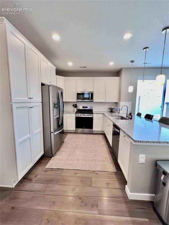Image 7 of 20: Kitchen featuring wood-finish flooring, white cabinetry, stainless steel ap