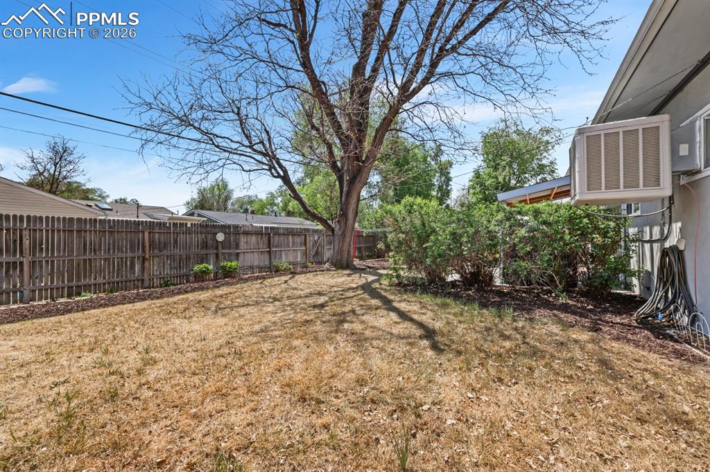 Image 26 of 27: Fenced yard with mature trees and shrubs.