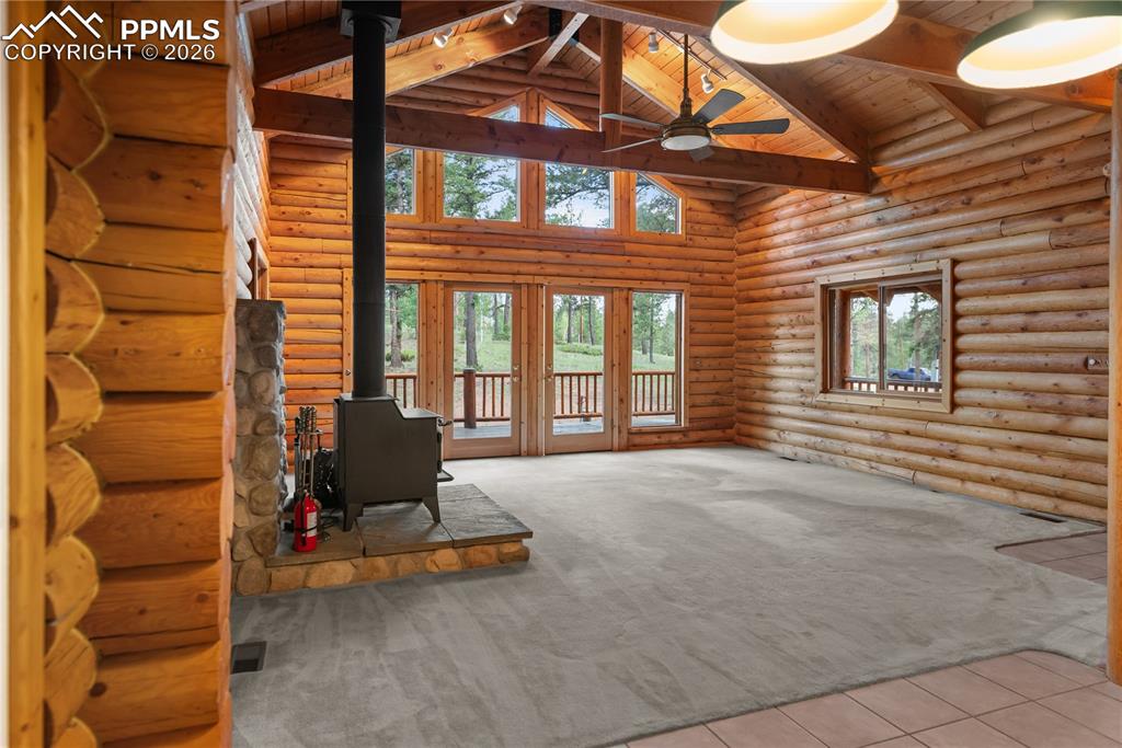 Image 11 of 45: Unfurnished living room featuring a wood stove, log walls, high vaulted cei