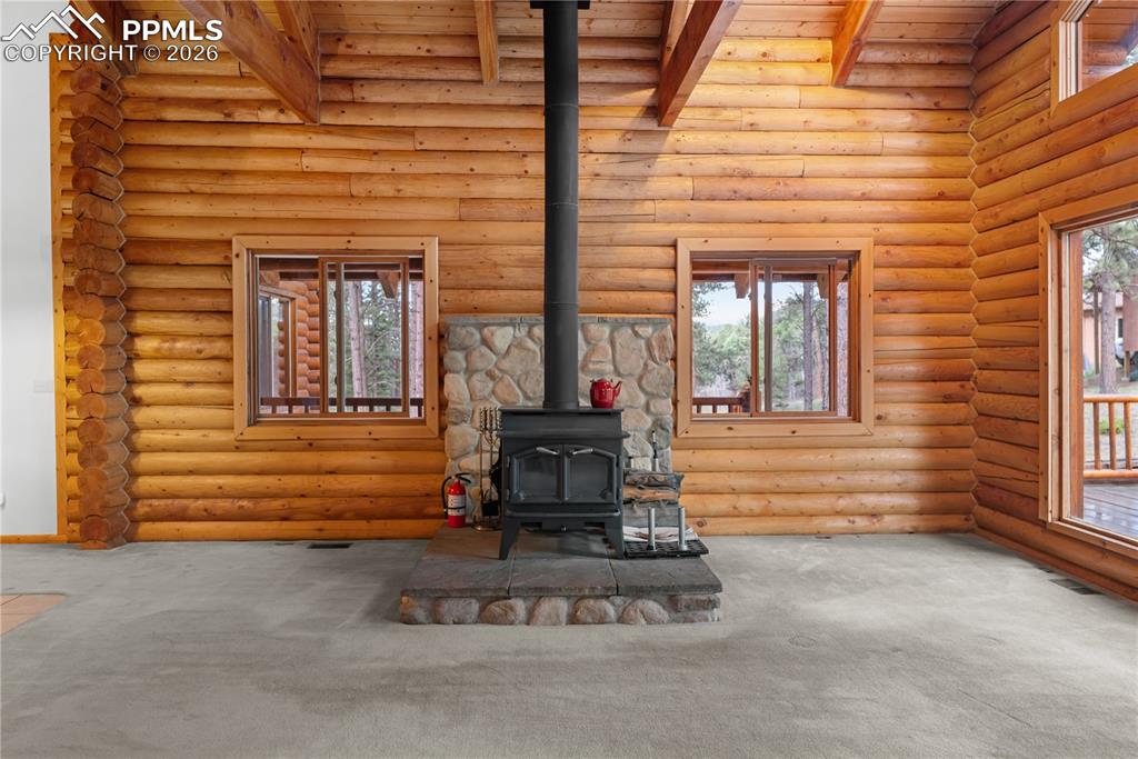 Image 12 of 45: Unfurnished living room featuring a wood stove, carpet, log walls, and a wo