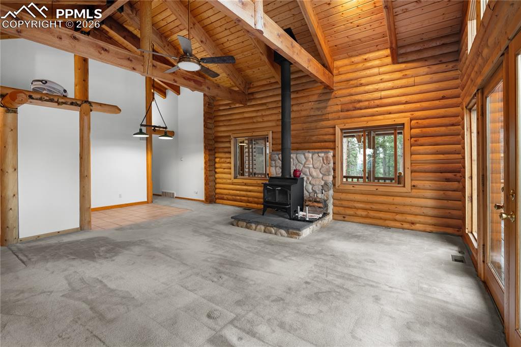 Image 13 of 45: Unfurnished living room with a wood stove, a wooden ceiling with exposed be