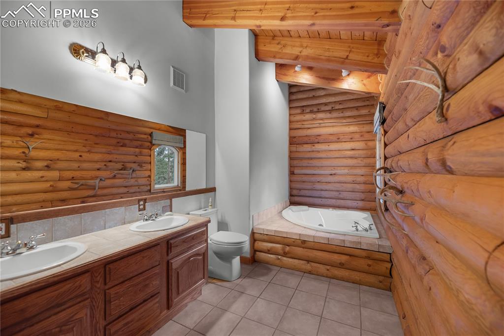 Image 23 of 45: Full bath with log walls, a garden tub, double vanity, tile patterned floor