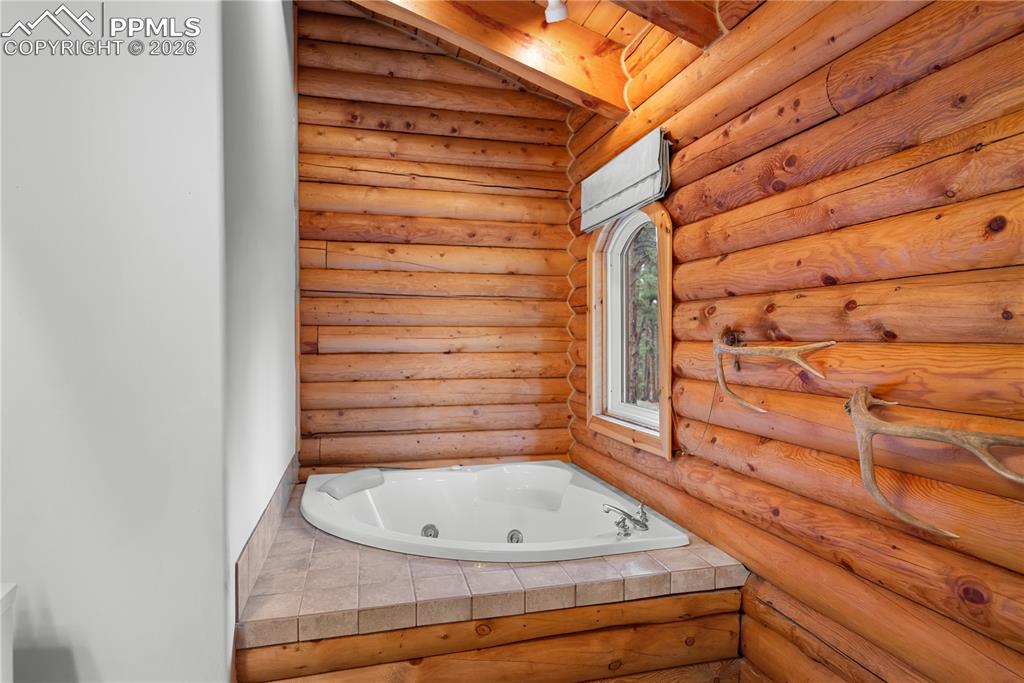 Image 24 of 45: Full bath featuring a jetted tub, log walls, and beam ceiling