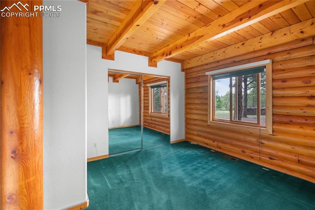 Image 25 of 45: Empty room with rustic walls, a wooden ceiling with exposed beams, and carp