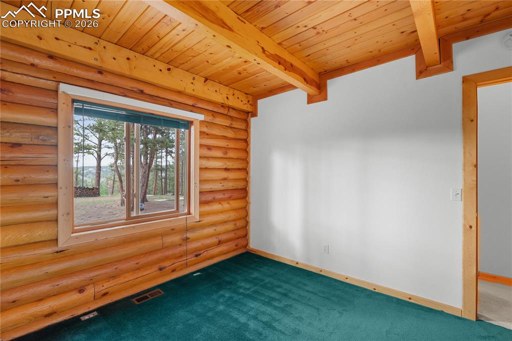 Image 26 of 45: Empty room featuring rustic walls, a wood ceiling with exposed beams, and d