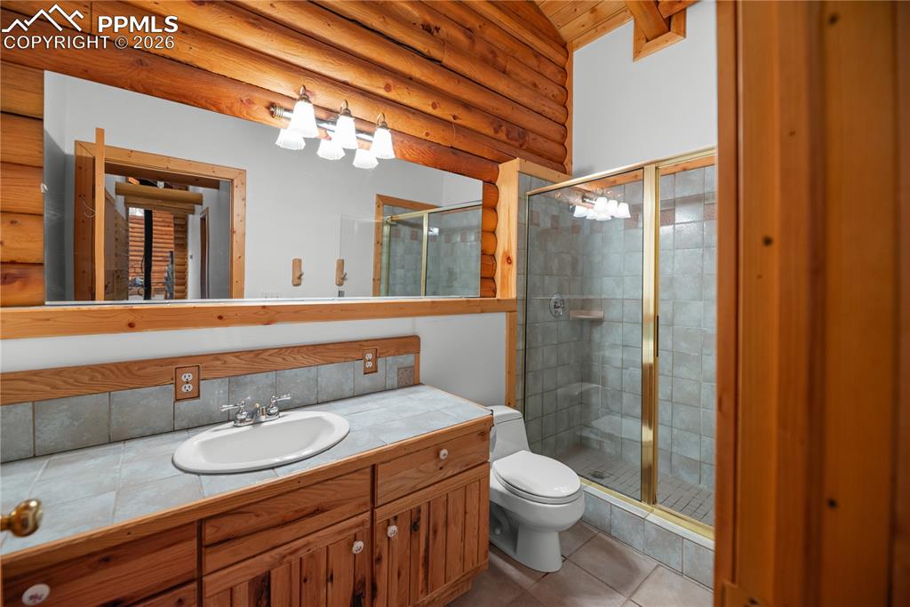 Image 27 of 45: Bathroom with log walls, vanity, a stall shower, tile patterned floors, and