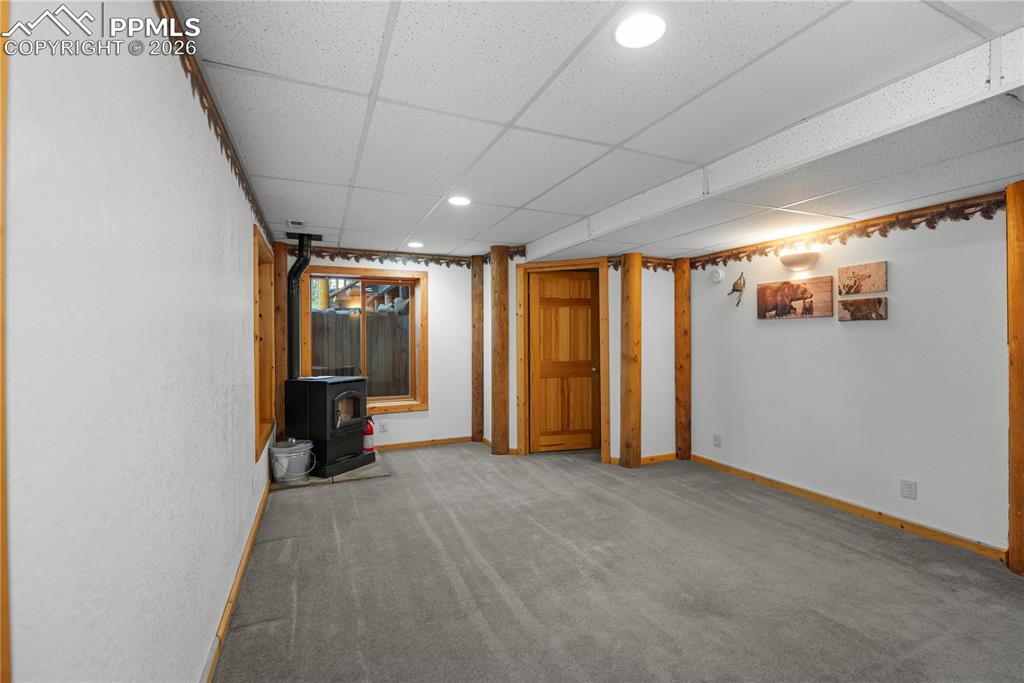 Image 32 of 45: Unfurnished living room featuring a wood stove, a drop ceiling, carpet, and