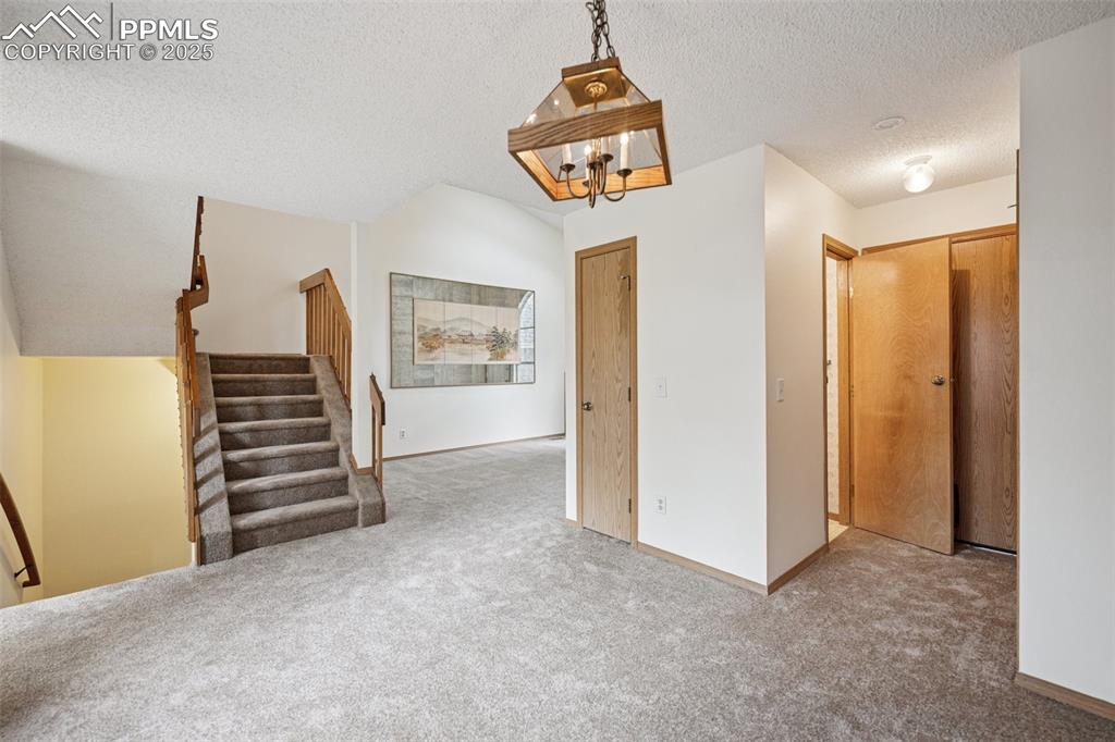 Image 10 of 48: Hallway with a textured ceiling, carpet, a chandelier, and stairway