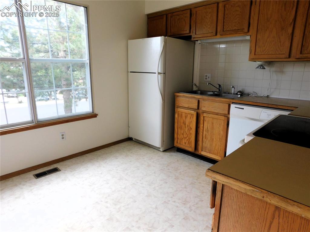 Image 11 of 48: Kitchen featuring brown cabinetry, backsplash, white appliances, and light 