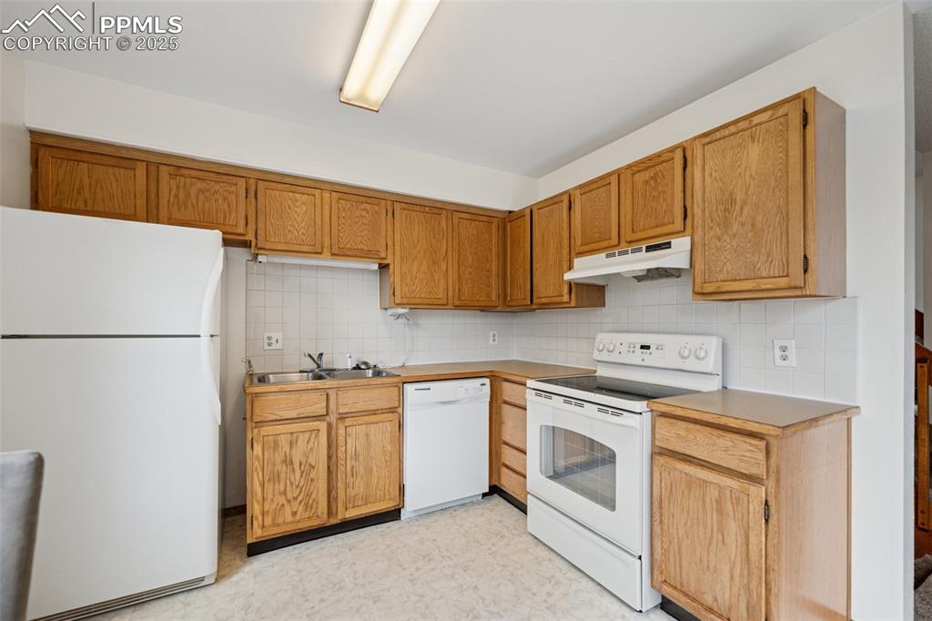 Image 12 of 48: Kitchen featuring white appliances, decorative backsplash, light floors, un