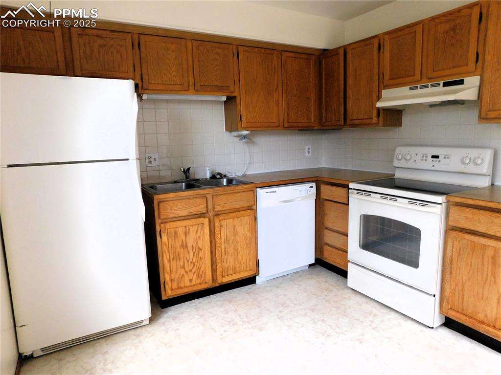 Image 13 of 48: Kitchen featuring white appliances, backsplash, under cabinet range hood, a