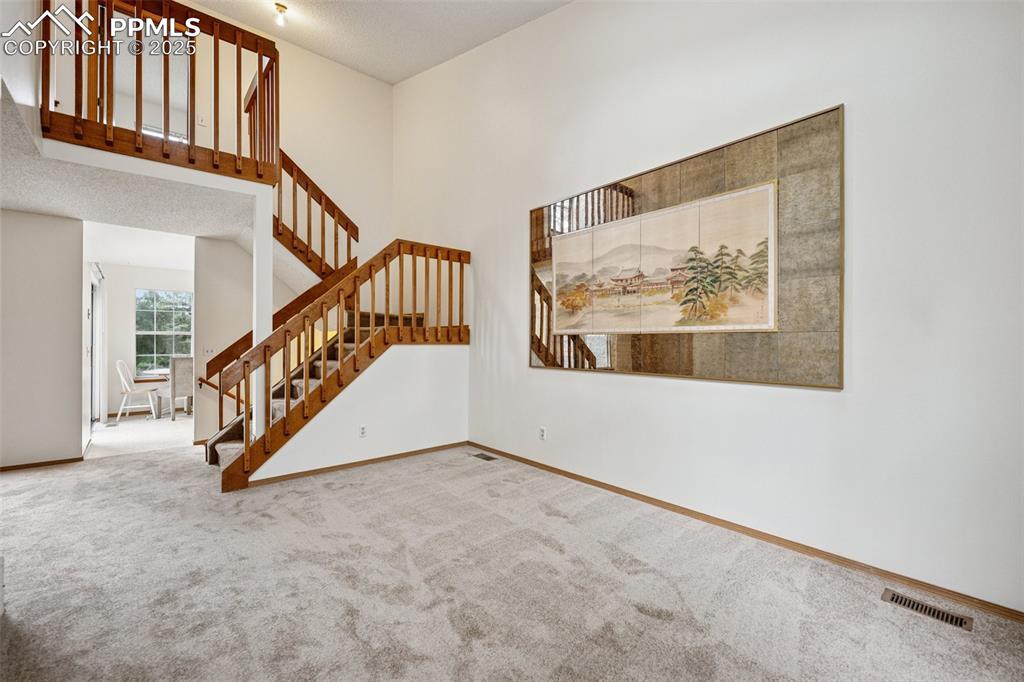 Image 3 of 48: Unfurnished living room featuring a towering ceiling, carpet, stairway, and