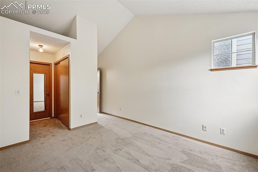 Image 36 of 48: Carpeted empty room featuring vaulted ceiling and a textured ceiling