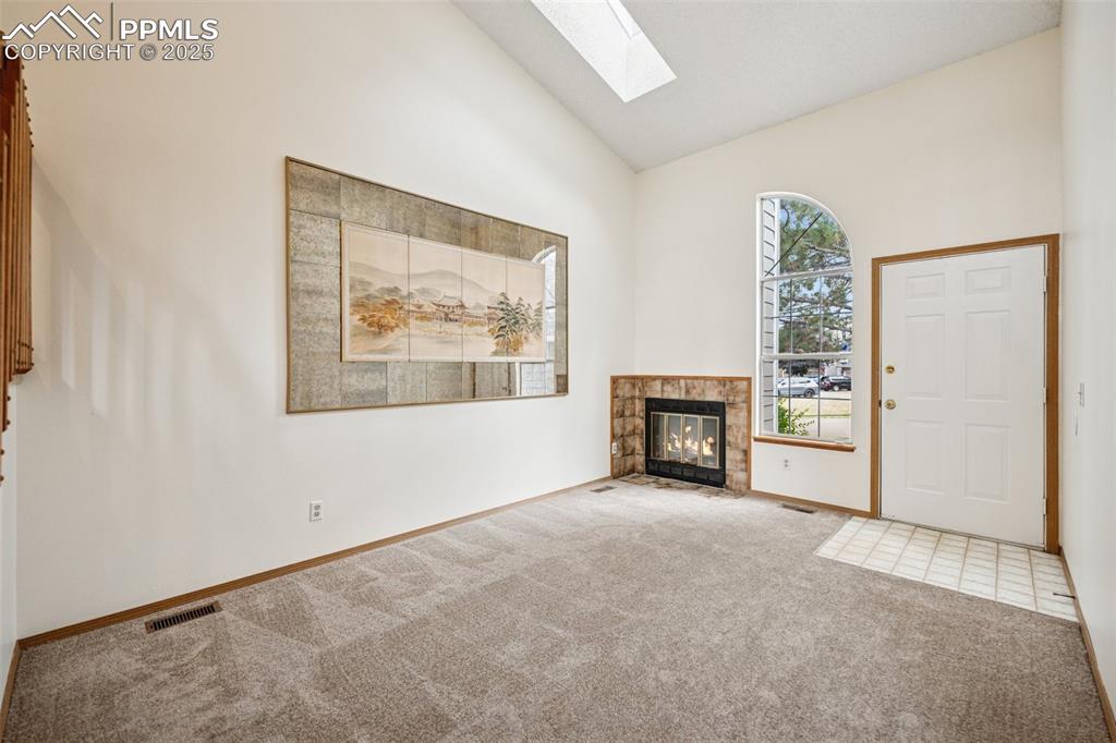 Image 5 of 48: Unfurnished living room with a skylight, carpet, high vaulted ceiling, and 