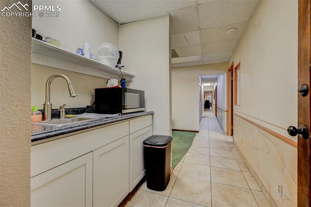 Image 37 of 45: Kitchen with a paneled ceiling, a sink, white cabinetry, dark countertops,