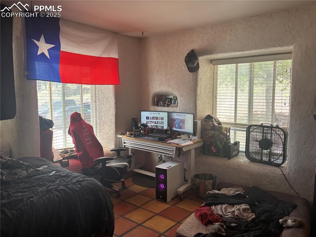 Image 13 of 25: Bedroom with a textured wall, multiple windows, and tile patterned flooring