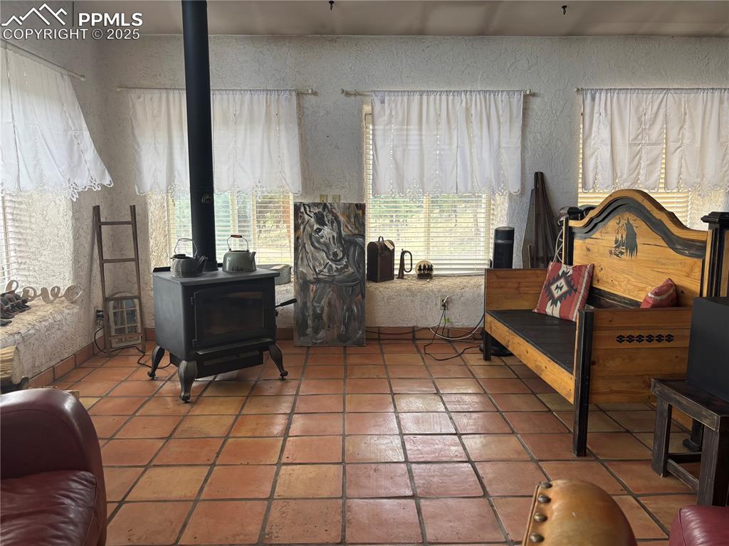 Image 5 of 25: Living area with a textured wall, a wood stove, and tile patterned flooring
