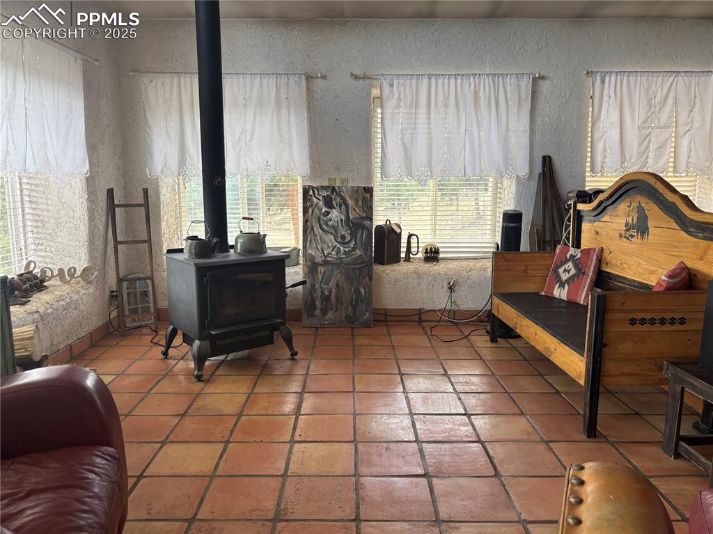 Image 6 of 25: Sitting room with a wood stove, a textured wall, and tile patterned floorin