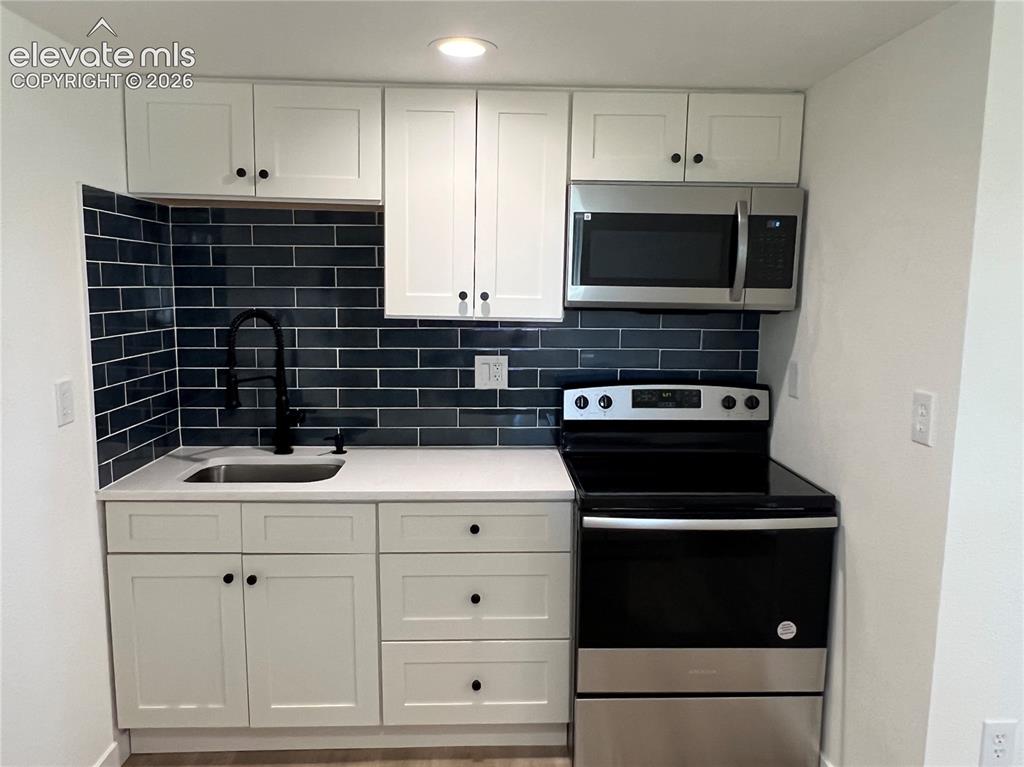 Image 15 of 23: Cottage - White shaker cabinetry, dark blue subway tile backsplash, stainle