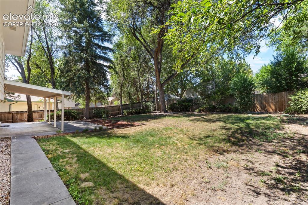 Image 13 of 39: The spacious backyard, fully fenced and shaded by mature trees, will be an 