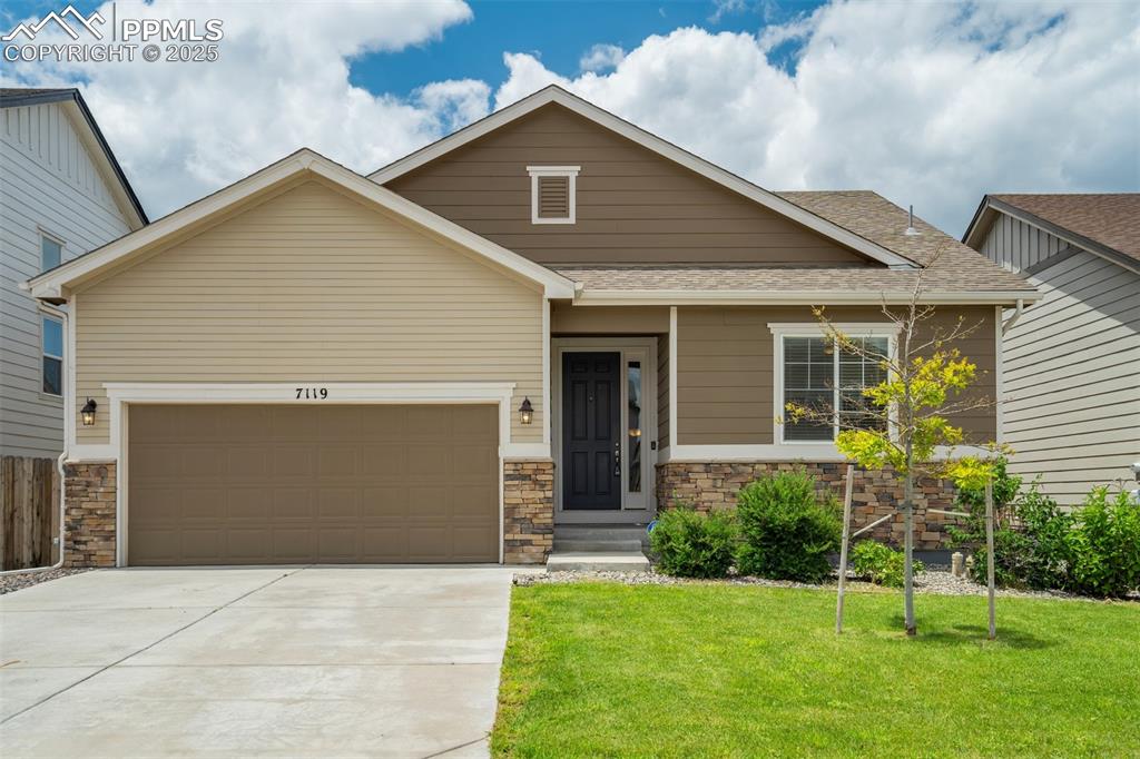 Caption: View of front of property featuring stone siding, concrete driveway, a front yard, a garage, and roo