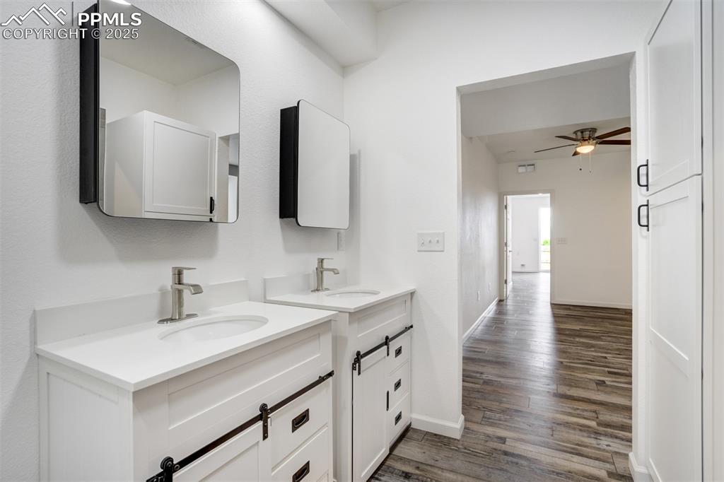 Image 35 of 44: Bathroom with wood finished floors, two vanities, and a ceiling fan