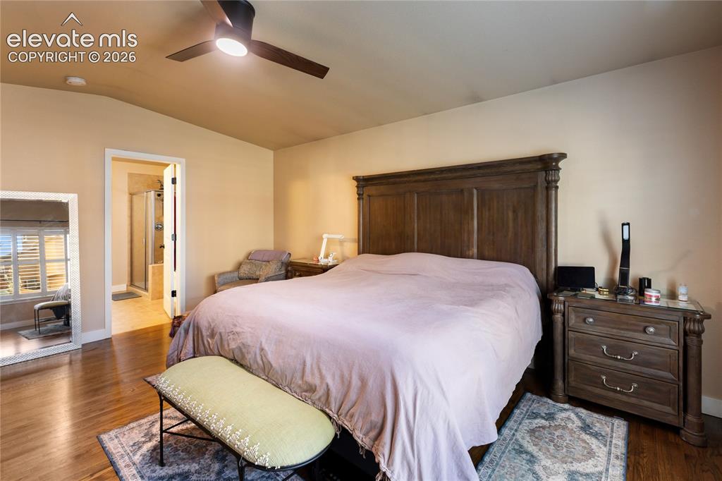 Image 11 of 29: Wood-finish flooring, vaulted ceiling, and an attached bathroom with a glas