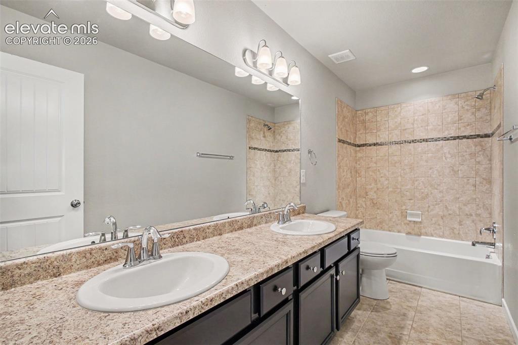 Image 23 of 39: Bathroom featuring a dual-sink vanity with a speckled countertop, dark wood