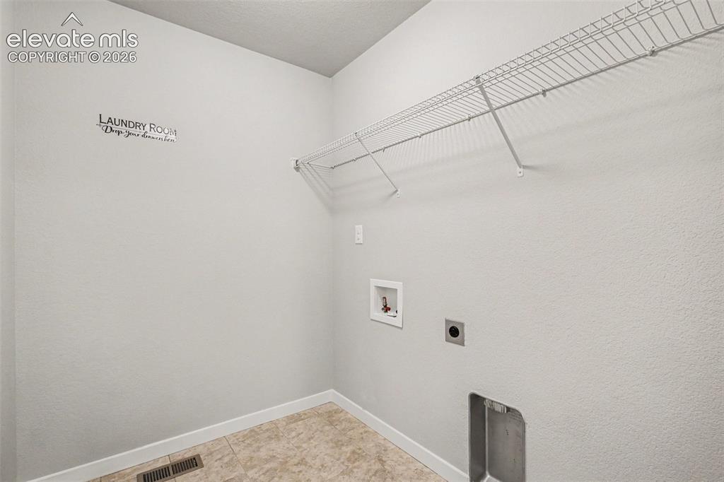 Image 27 of 39: Dedicated laundry area featuring a wire storage shelf, tiled flooring, and