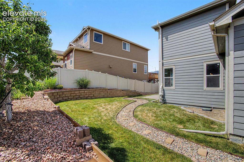 Image 35 of 39: Manicured backyard featuring a stone pathway, tiered landscaping with a ret