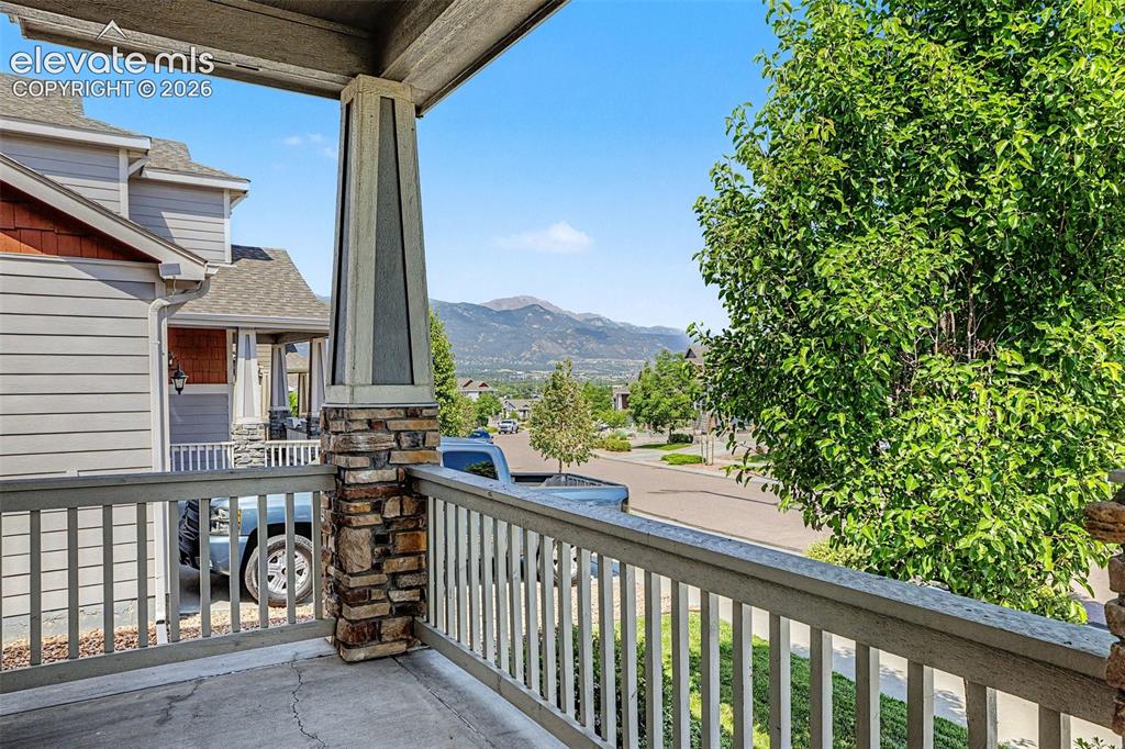 Image 4 of 39: Covered porch with stone column base, wood railing, and distant mountain sc