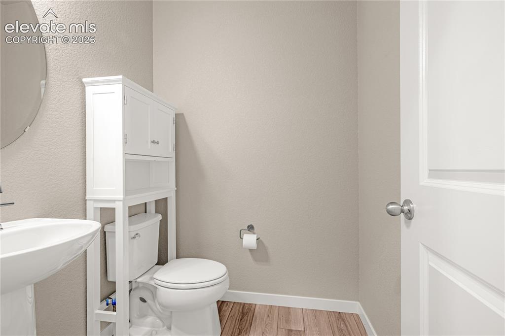 Image 9 of 30: Pedestal sink with a circular mirror, wood-finish flooring, and a white bui