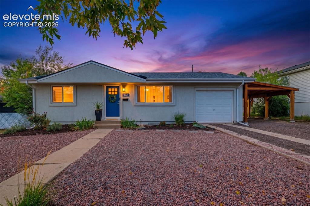 Caption: Exterior featuring a covered carport, attached garage, concrete pathway, and decorative gravel lands