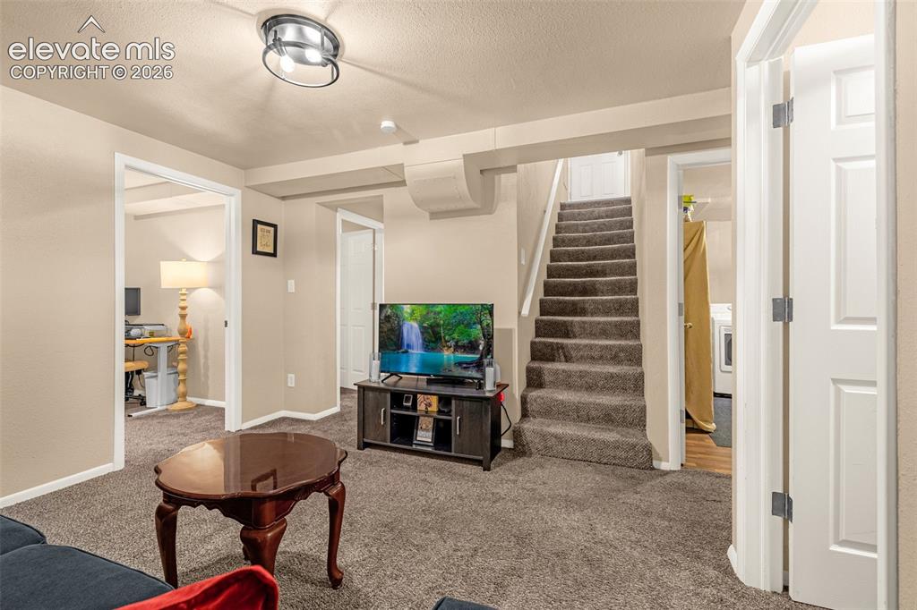 Image 12 of 27: Carpeted family room with a staircase to the main level, and access to addi