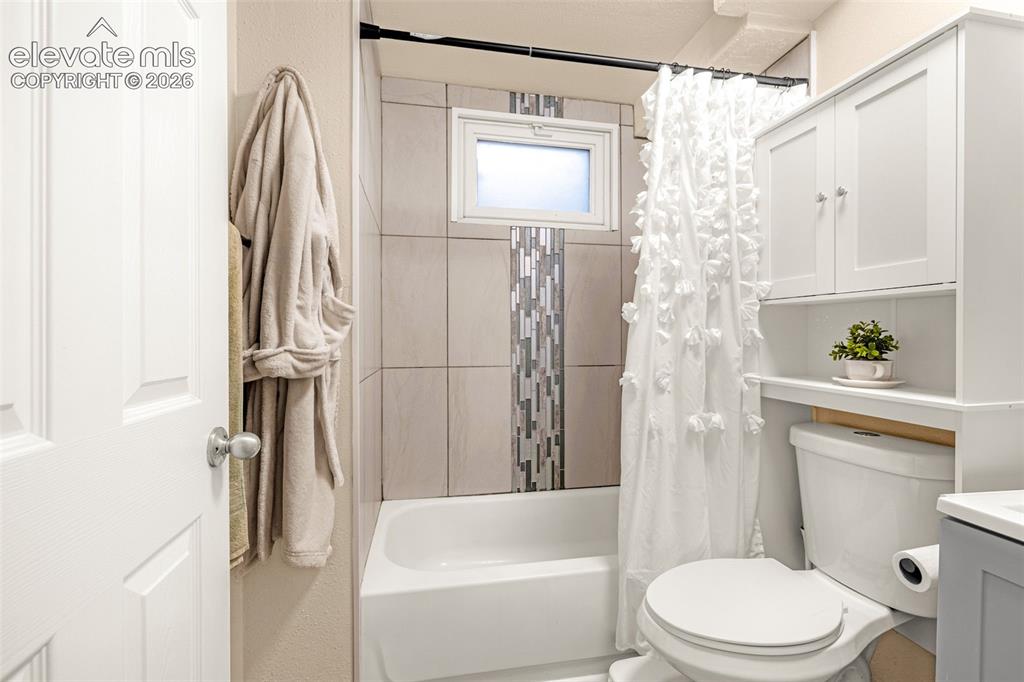 Image 15 of 27: White bathtub and shower combination with a tile surround, mosaic accent st