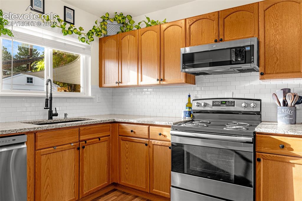 Image 4 of 27: Kitchen featuring wood cabinetry, stainless steel appliances, granite count